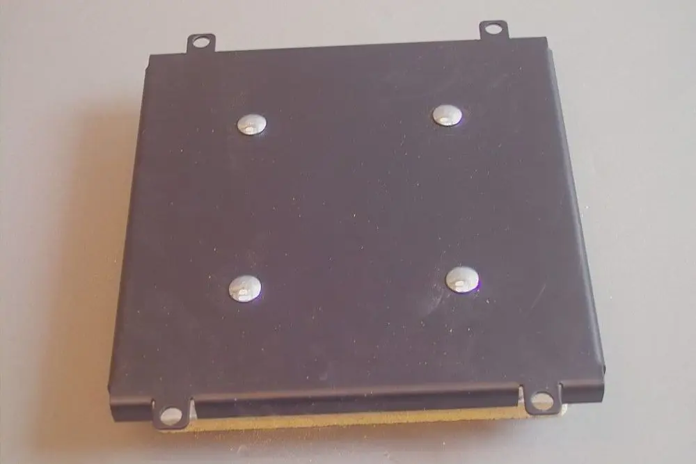 Blick auf einen rechteckigen, schwarzen Deckel mit vier Schrauben. Der Deckel zeigt Spuren von Gebrauch und ist für einen Brötje-Brennkammeraufbau konzipiert.