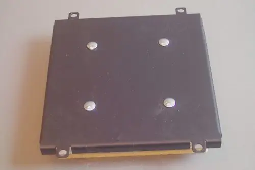 Blick auf einen rechteckigen, schwarzen Deckel mit vier Schrauben. Der Deckel zeigt Spuren von Gebrauch und ist für einen Brötje-Brennkammeraufbau konzipiert.