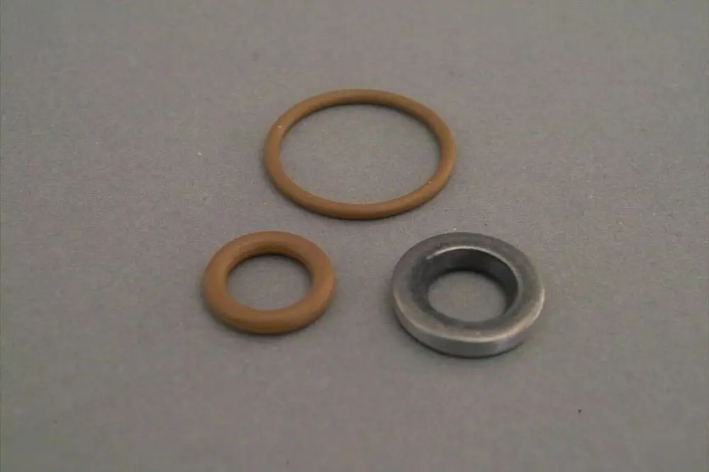 Drei Dichtungsringe in verschiedenen Größen, zwei aus Gummi in Braun und einer aus Metall, angeordnet auf einem grauen Untergrund, möglicherweise von Brötje.
