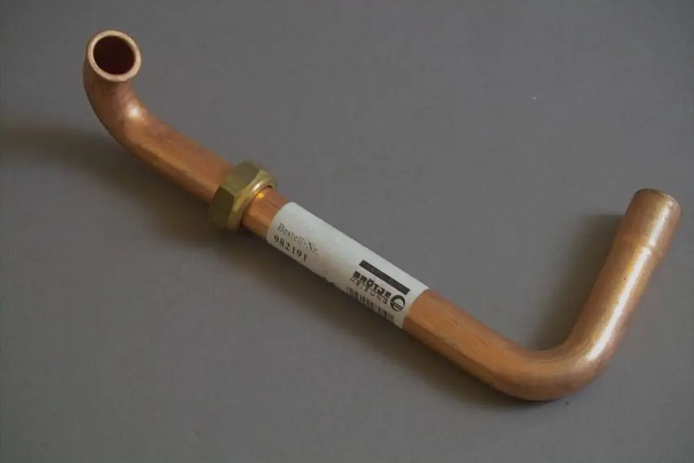 Kupfernes Rücklaufrohr von Brötje mit einer gebogenen Form und einer Verschraubung aus Messing. Fittings sind nicht klar erkennbar.
