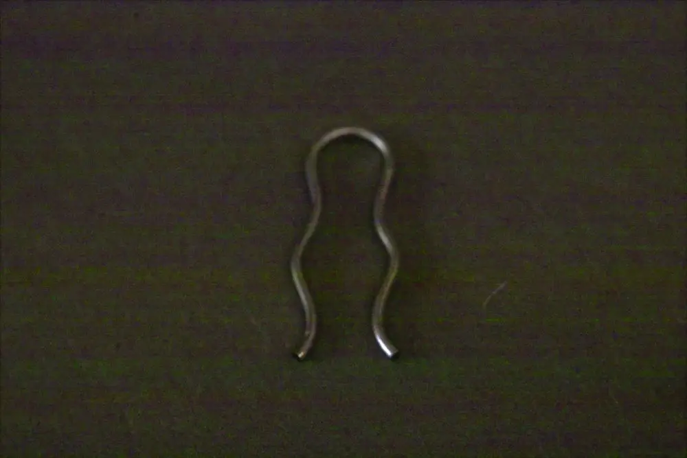 Brötje Klammer in geschwungener Form, aus Metall mit offenen Enden. Das Produkt liegt auf einem dunklen Hintergrund und zeigt eine einfache, funktionale Konstruktion.