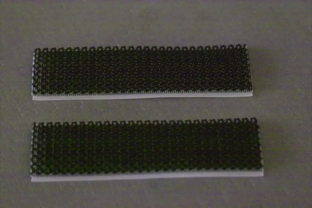 Zwei schwarze Klettstreifen auf einer grauen Oberfläche, deutlich erkennbar, ideal für Anwendungen von Brötje zur Befestigung oder Montage.