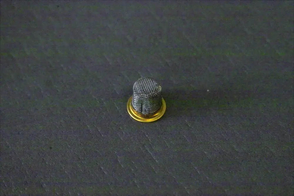 Kleiner runder Brötje-Filter mit feinem Netz und goldenem Rand auf schwarzem Hintergrund.