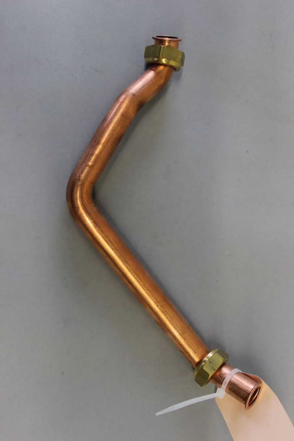 Kupferne Rücklaufverbindungsleitung mit einer gebogenen Form und Gewindeanschlüssen, angebracht mit einer Metallmutter, gekennzeichnet mit einem Etikett. Marke Brötje.