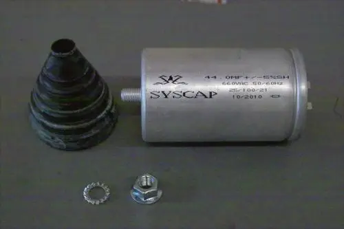 Kondensator von Brötje in zylindrischer Form, mit Metallgehäuse und Anschlussgewinde, neben einem konischen Gummi-Element und Metallverschlüssen auf grauem Hintergrund.