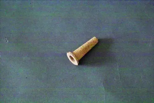 Ein Brötje Sinterfilter, zylindrisch mit einer perforierten Oberfläche, liegt auf einer grauen Unterlage.