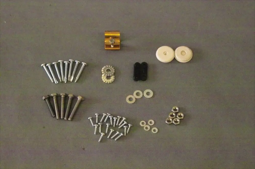 Schrauben-Set von Brötje, bestehend aus verschiedenen Schrauben, Unterlegscheiben, Riegeln und einem Bauteil in Gold, übersichtlich auf grauem Hintergrund angeordnet.