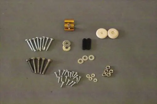 Schrauben-Set von Brötje, bestehend aus verschiedenen Schrauben, Unterlegscheiben, Riegeln und einem Bauteil in Gold, übersichtlich auf grauem Hintergrund angeordnet.