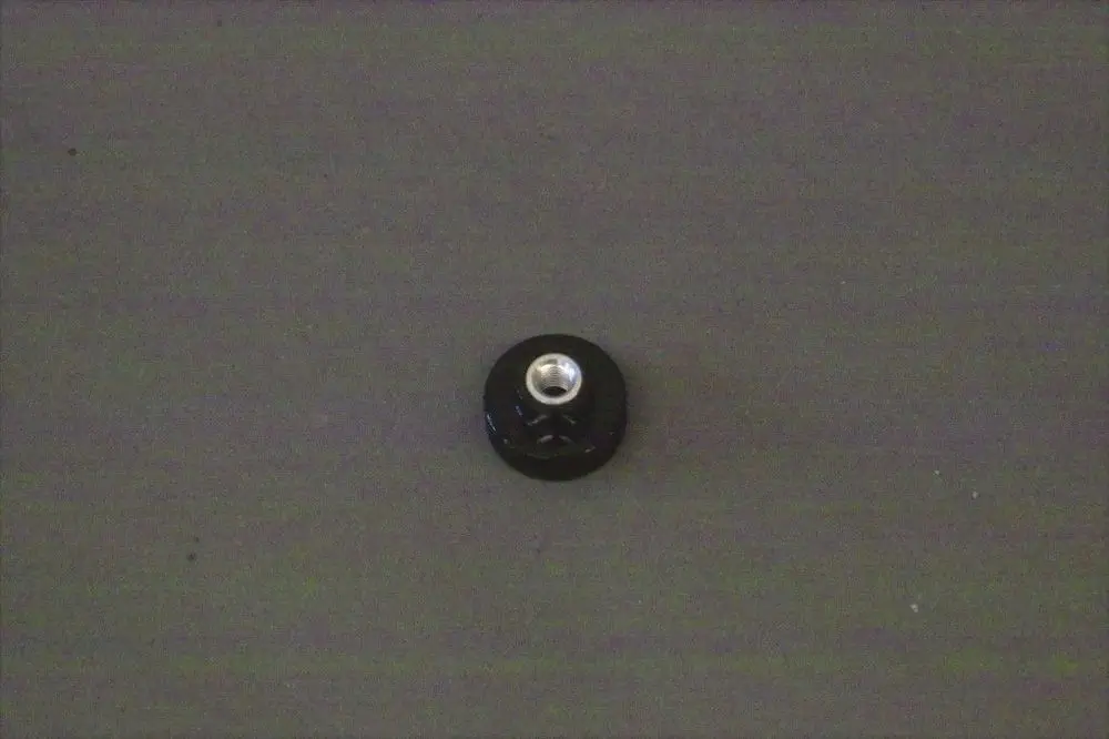 Schwarze Rändelhohlmutter mit metallischer Öffnung in der Mitte, auf grauem Untergrund. Produkt von Brötje.