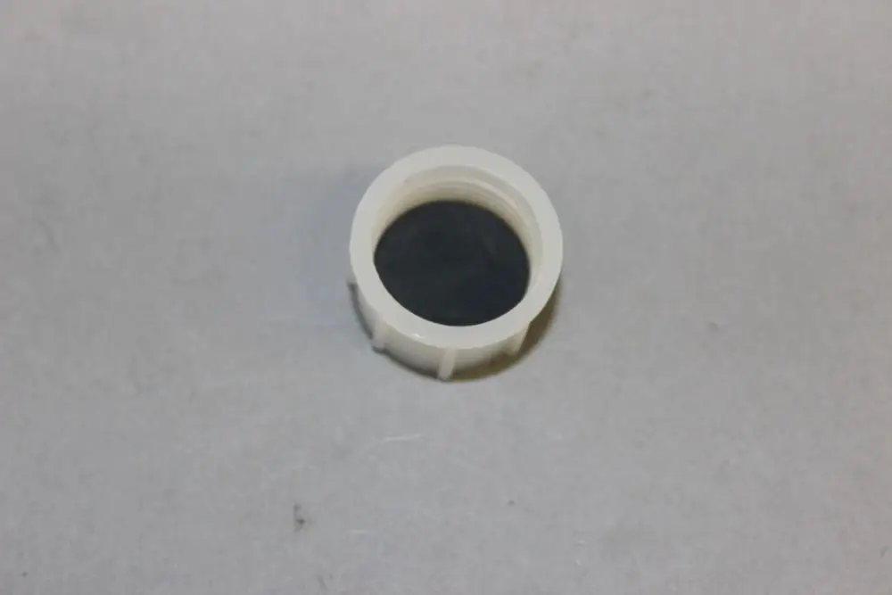 Brötje Schraubdeckel für Siphon in neutraler Farbe, runde Form mit innen liegendem schwarzen Einsatz, auf grauem Hintergrund platziert.