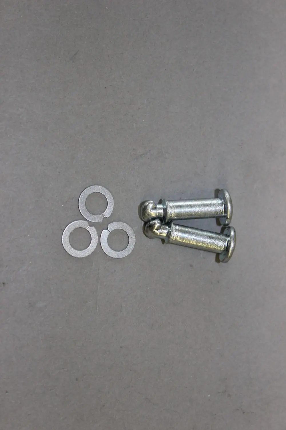 Zwei metallene Schnellverschluss-Schrauben mit runden Köpfen und drei Unterlegscheiben auf grauem Hintergrund, hergestellt von Brötje.