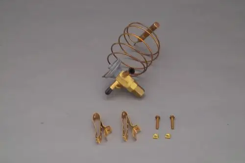 Brötje-Expansionsventil mit kupferner Spirale, Anschlussstück und Zubehörteilen, einschließlich Schrauben und Halterungen, auf grauem Hintergrund angeordnet.