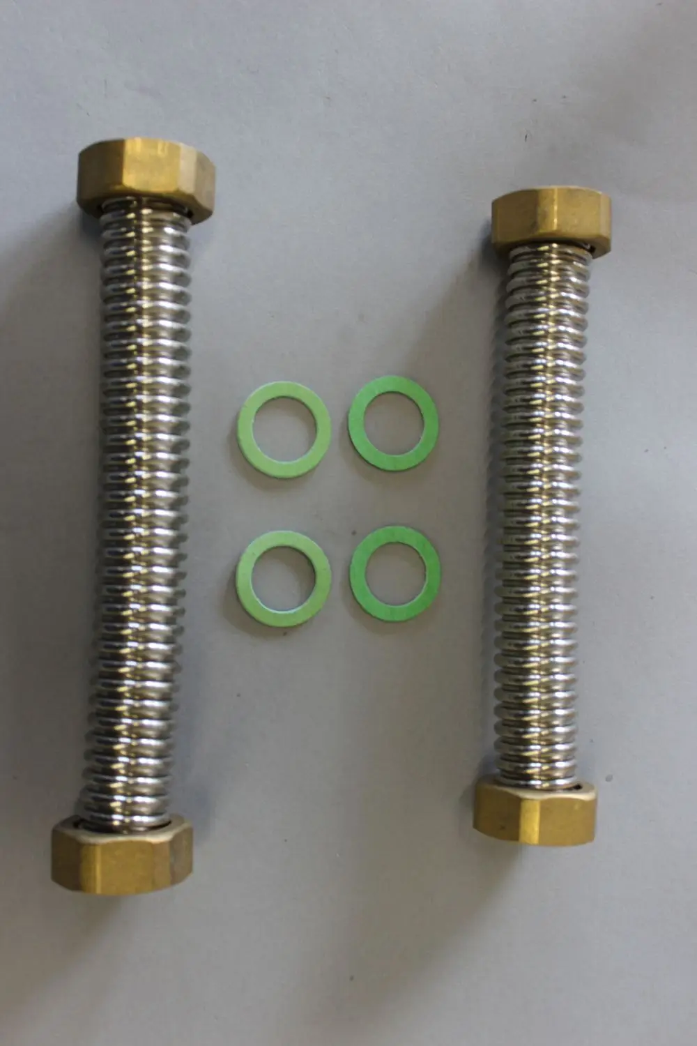 Zwei gerippte Metallbolzen mit sechseckigen Messingmuttern und vier grünen Unterlegscheiben auf einem hellen Untergrund. Das Montage-Set ist von Brötje.