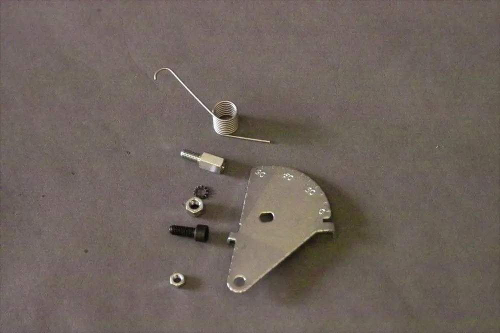 Brötje Scalensegment mit verschiedenen Metallteilen, darunter eine gebogene Feder, Schrauben und eine Metallplatte, auf grauem Untergrund angeordnet.