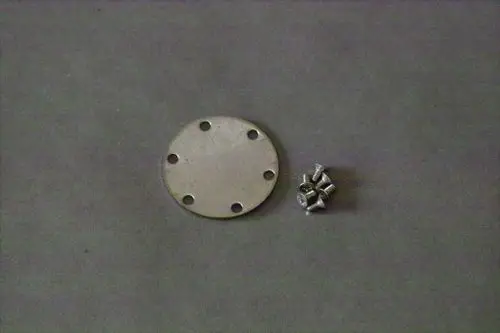 Metallplatte mit mehreren Befestigungslöchern und einer Gruppe von kleinen Schrauben, möglicherweise Teil eines Brötje Heizsystems.