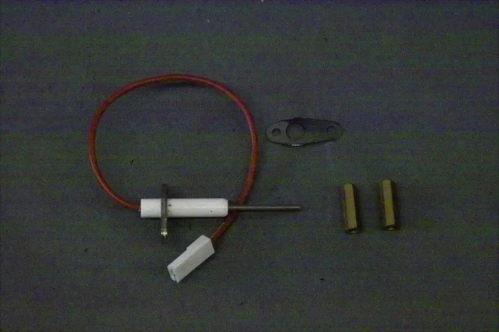 Brötje Ionisationselektrode mit einem weißen Kunststoffgehäuse und rotem Kabel, flankiert von zwei Messinghülsen und einer Montageplatte.