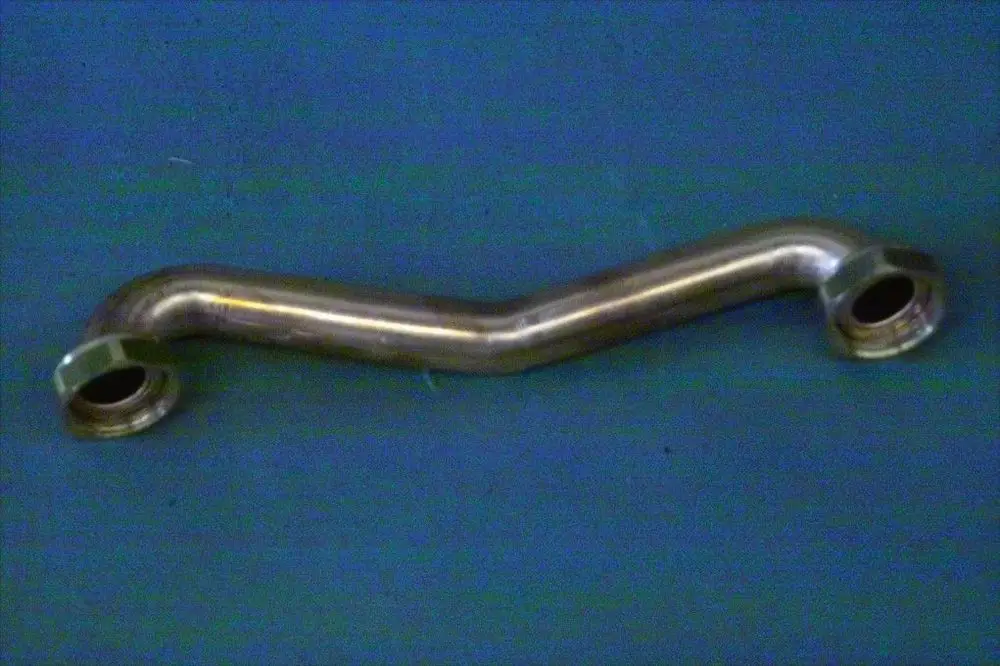 Verbindungsrohr von Brötje mit zwei Anschlüssen, leicht gebogen und aus Metall gefertigt, auf blauer Unterlage präsentiert.