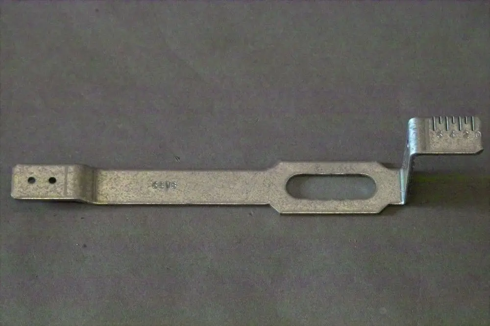 Brötje Halter mit einer flachen Metallkonstruktion, einer seitlichen Ausbuchtung und einer geriffelten Kante für Montagezwecke, auf grauem Hintergrund.