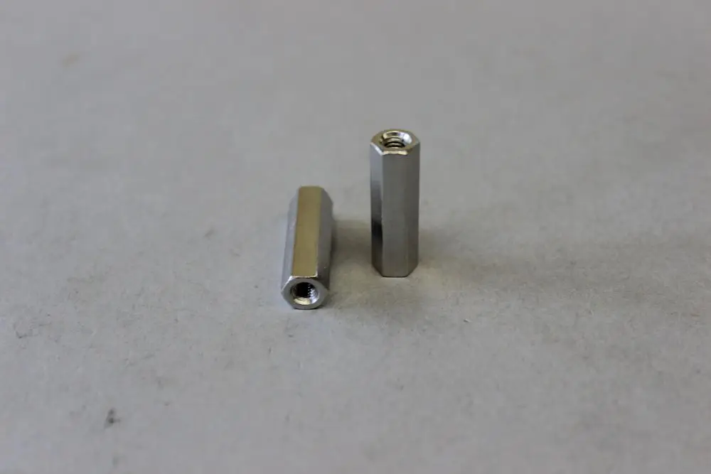 Zwei metallische, längliche Teile mit innenliegender Gewindebohrung, die möglicherweise als Verbindungselemente dienen, sind auf grauem Untergrund abgebildet. Brötje-Produkt.