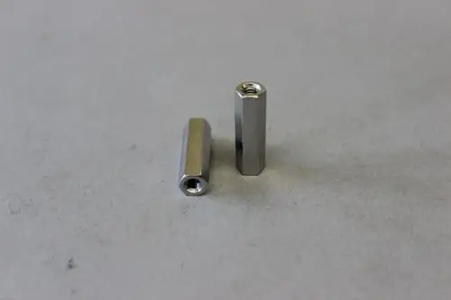 Zwei metallische, längliche Teile mit innenliegender Gewindebohrung, die möglicherweise als Verbindungselemente dienen, sind auf grauem Untergrund abgebildet. Brötje-Produkt.
