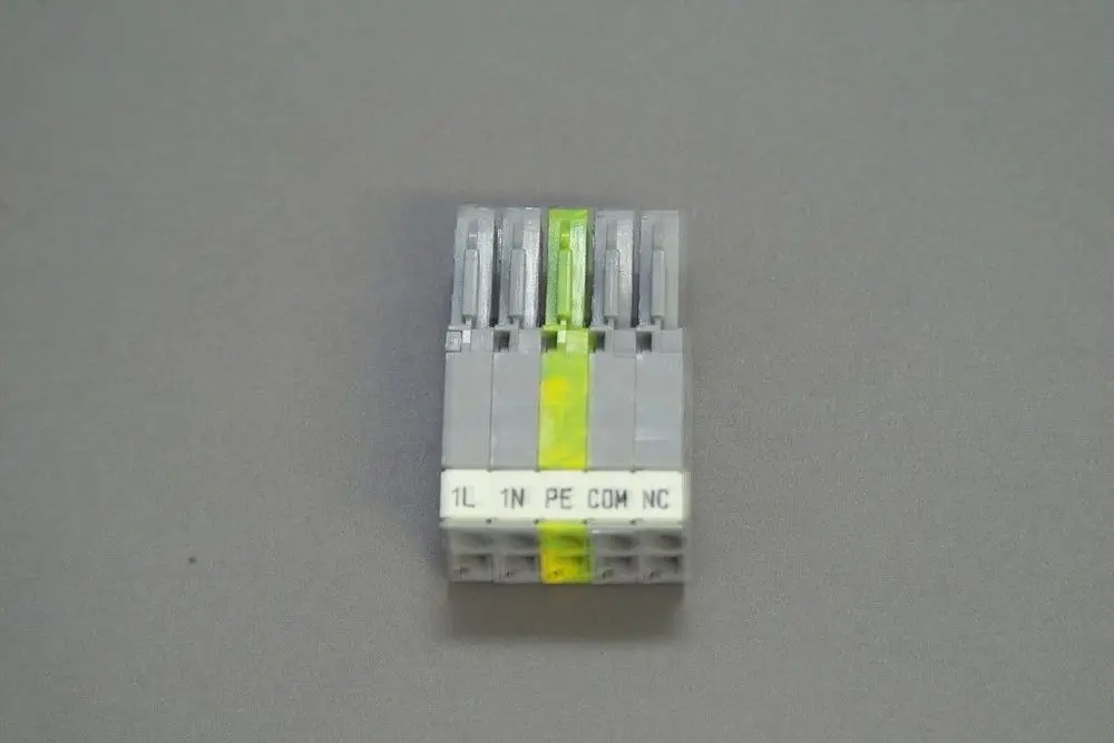 Brötje Stecker mit fünf Anschlüssen, erkennbar an der farbigen Kennzeichnung und den Anschlussbezeichnungen wie 1L, 1N, PE, COM, NC auf grauem Untergrund.