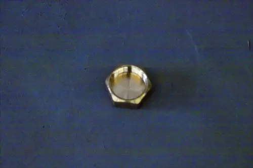 Brötje-Kappe aus Metall mit sechseckiger Form und glatter Innenseite, auf einer grauen Unterlage platziert.