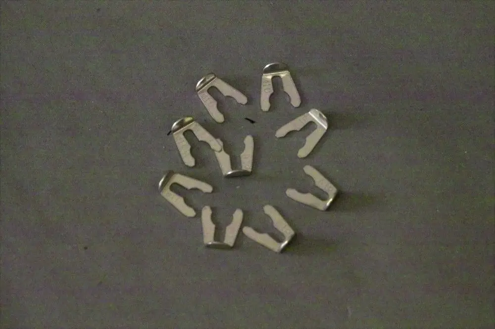 Metallene Arretierclips in Form von U-Objekten, angeordnet in einem kreisförmigen Muster auf dunklem Hintergrund, geeignet für Rohrverbindungen, Marke Brötje.
