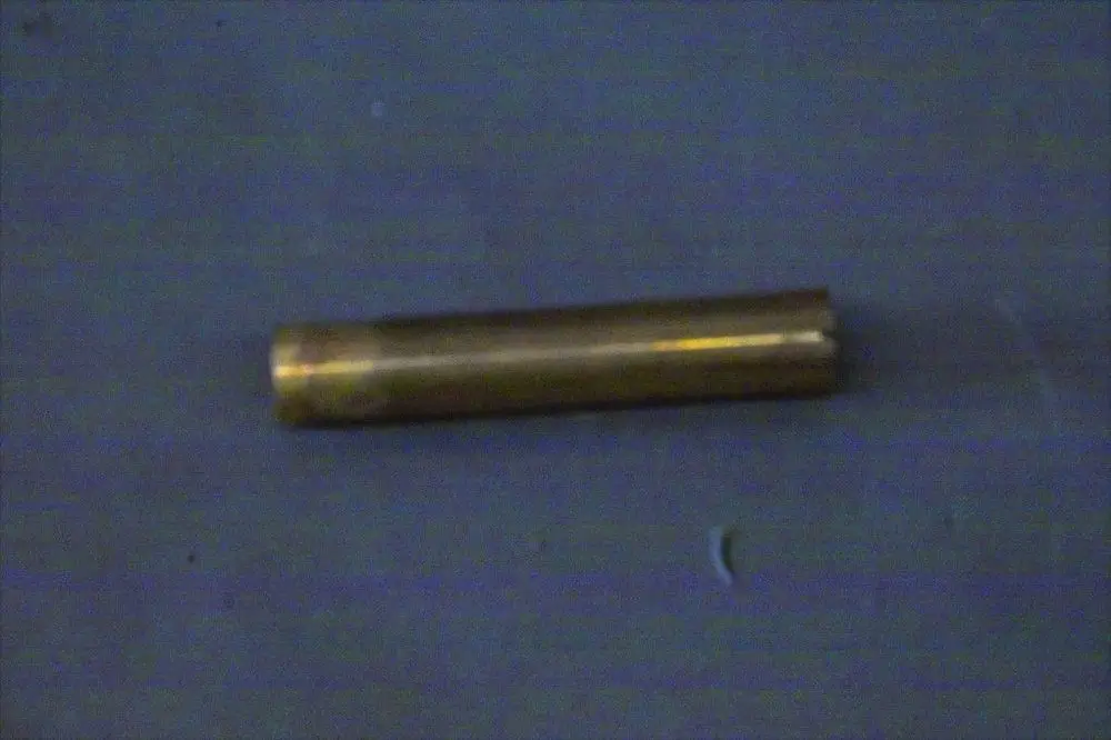 Ein zylindrischer, messingfarbener Metallkörper, möglicherweise ein Verbindungselement, liegt auf einer blauen Oberfläche. Er könnte Bestandteil eines Brötje-Heizsystems sein.