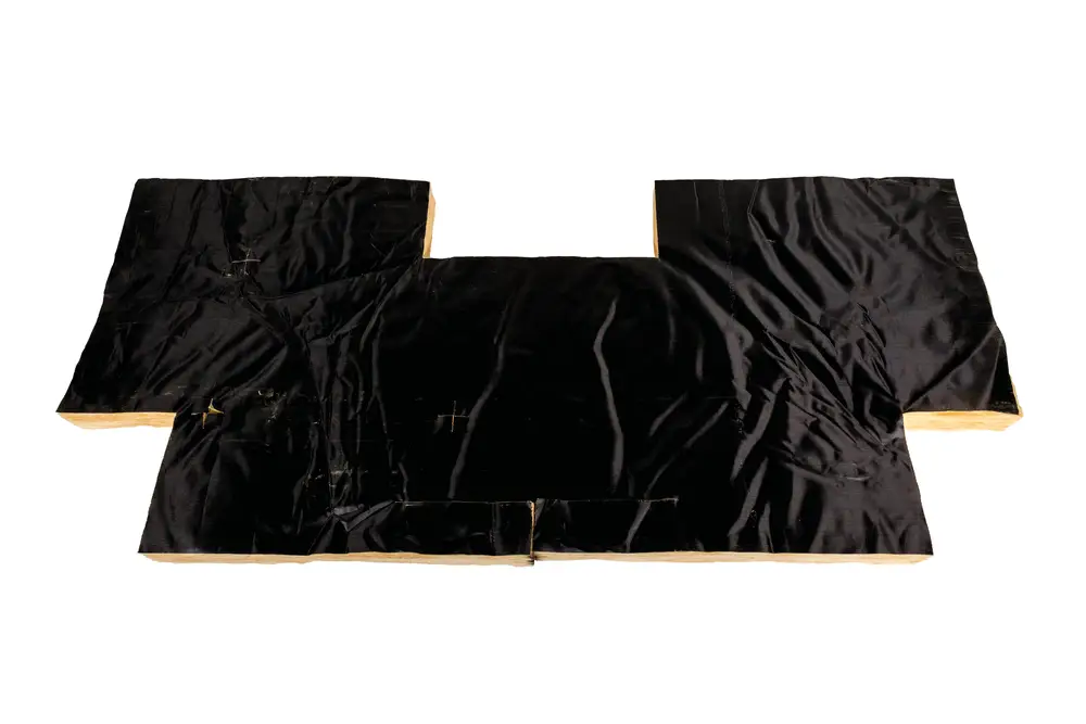 Schwarze Iso-Matte von Brötje, flache Form mit Naht und Falten. Material sieht nach Stoff mit kompaktem Bezug aus. Verwendung möglicherweise im Heizungsbereich.