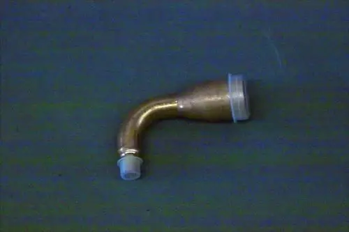 Eingeknickte Einspritzleitung aus Messing mit transparentem Endstück, auf einer unifarbenen Unterlage. Produkt von Brötje zur Verwendung in Heizsystemen.