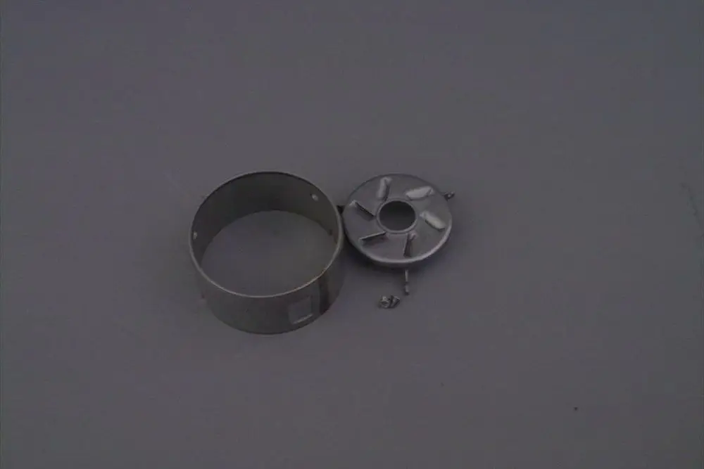 Brötje Flammenkopf aus Metall mit runder Satuscheibe, die an einer Seite eine Öffnung hat. Beide Teile liegen auf einer grauen Fläche.