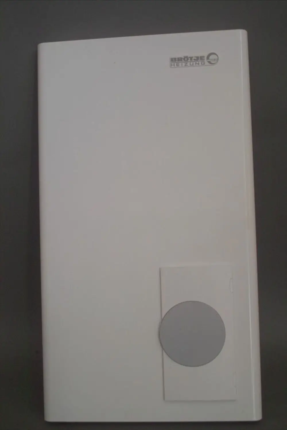Weiße, flache Abdeckung mit einem Kreisrahmen auf der Vorderseite, versehen mit dem Logo der Marke Brötje.