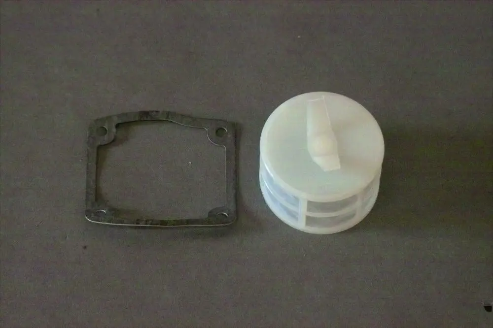 Brötje Pumpenfilter und Dichtung in zwei Teilen, der Filter hat eine runde Form mit horizontalen Rillen, die Dichtung ist rechteckig mit abgerundeten Ecken und Bohrungen.