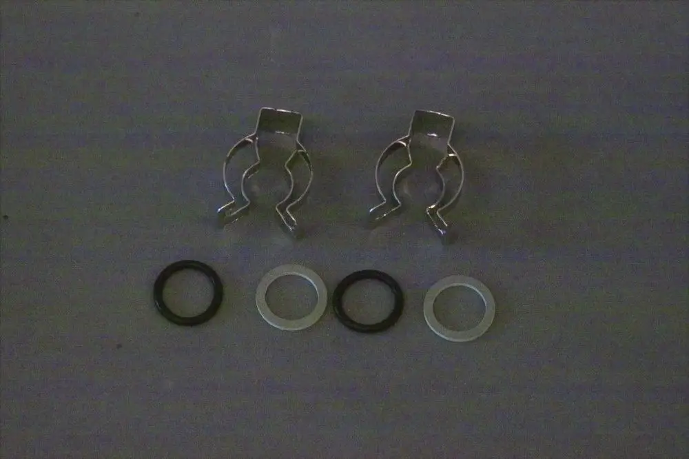 Zwei metallische Clips und drei Gummi-O-Ringe in unterschiedlichen Farben, möglicherweise für die Installation von Brötje-Produkten.