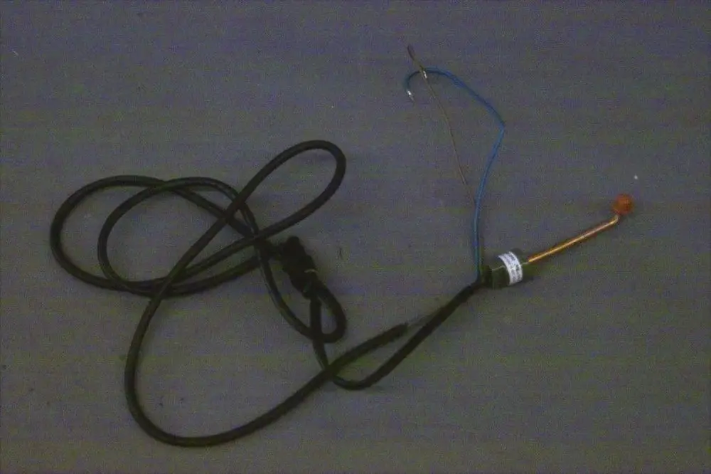 Schalter von Brötje mit einem Kabel und einer senkrechten Elektrode. Die Anschlussdrähte sind teilweise sichtbar. Der Schalter hat eine Kennzeichnung und eine orangefarbene Spitze.