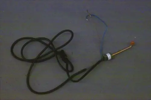 Schalter von Brötje mit einem Kabel und einer senkrechten Elektrode. Die Anschlussdrähte sind teilweise sichtbar. Der Schalter hat eine Kennzeichnung und eine orangefarbene Spitze.