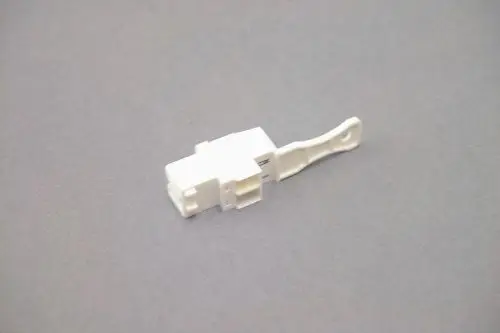 Weißer Stecker von Brötje, mit einem mittleren Gehäuse und einer Verbindungslasche, auf grauem Untergrund.