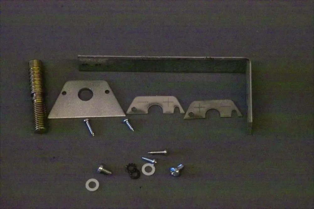 Verschiedene Metall- und Schraubenteile, einschließlich Halterungen und Unterlegscheiben, auf einem dunklen Untergrund, möglicherweise für ein Brötje Produkt.