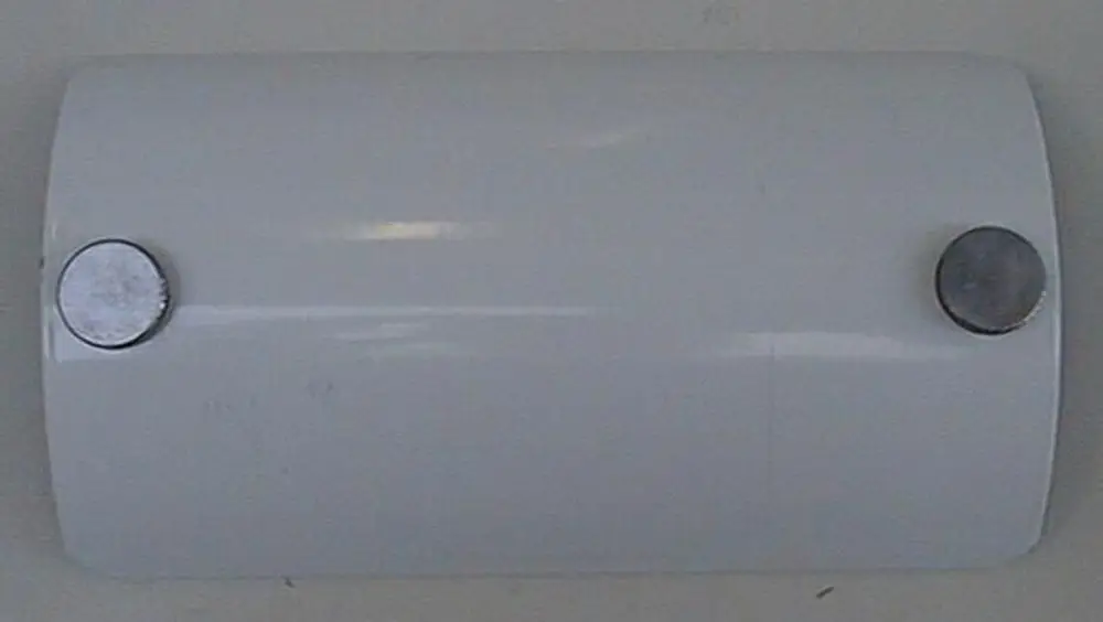 Weißer runder Deckel mit zwei Metallknöpfen, möglicherweise für eine Revisionsöffnung, Hersteller Brötje. Auf glatter Oberfläche, schlichtes Design.