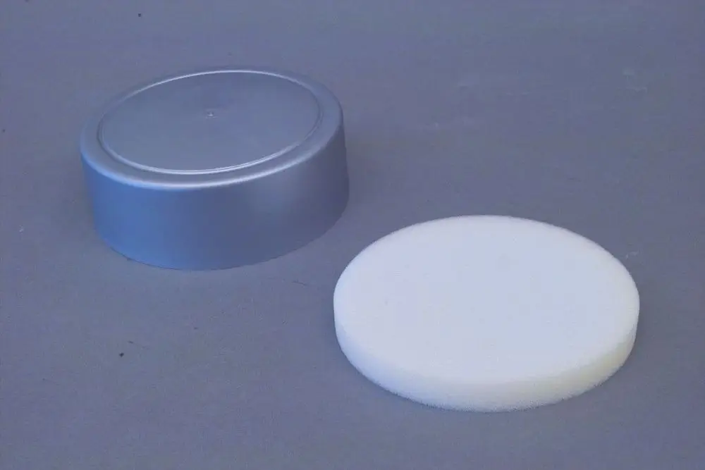 Brötje Flanschabdeckung in Silber, rund. Auf der linken Seite eine graue Abdeckung und rechts ein weißer, runder Schaumstoffring.