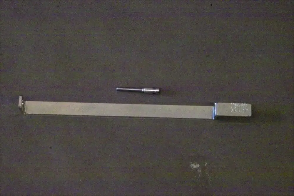 Brötje Düsenstock Halterung aus Metall mit einem flachen Arm und einem separaten kleinen Aufsatz, auf einem dunklen Untergrund abgebildet.