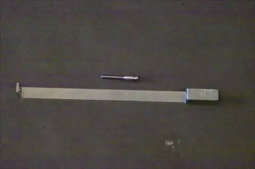 Brötje Düsenstock Halterung aus Metall mit einem flachen Arm und einem separaten kleinen Aufsatz, auf einem dunklen Untergrund abgebildet.