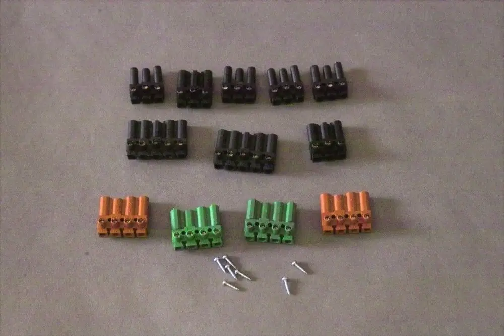 Brötje Steckverbinder in verschiedenen Farben (schwarz, orange, grün) angeordnet auf hellem Hintergrund, mit einigen Schrauben in der Nähe.