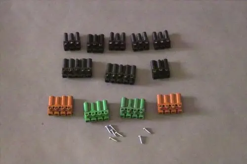 Brötje Steckverbinder in verschiedenen Farben (schwarz, orange, grün) angeordnet auf hellem Hintergrund, mit einigen Schrauben in der Nähe.