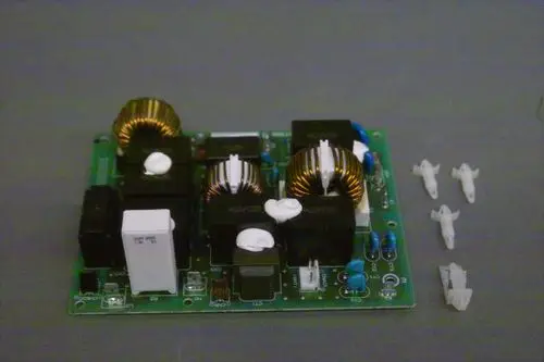 Brötje Elektronikfilterplatine mit mehreren Bauteilen, darunter Spulen und Schalter, auf einer grünen Leiterplatte. Neben der Platine sind mehrere weiße Clips angeordnet.