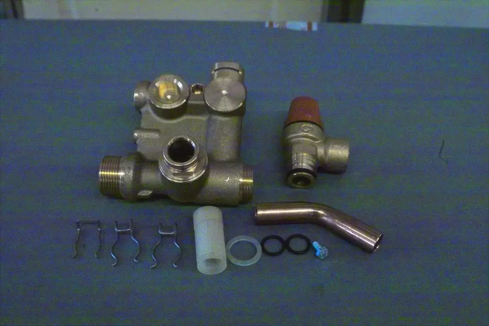 Brötje Hydraulikblock mit verschiedenen Verbindungselementen, darunter Rohre, Dichtungen und Halteclips, auf einem grauen Untergrund.