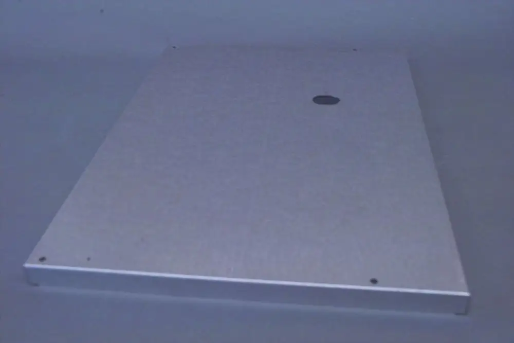 Aluminiummantel für Brötje Produkt, rechteckige Form mit einem runden Ausschnitt und mehreren kleinen Bohrungen an der Kante, auf grauem Hintergrund platziert.