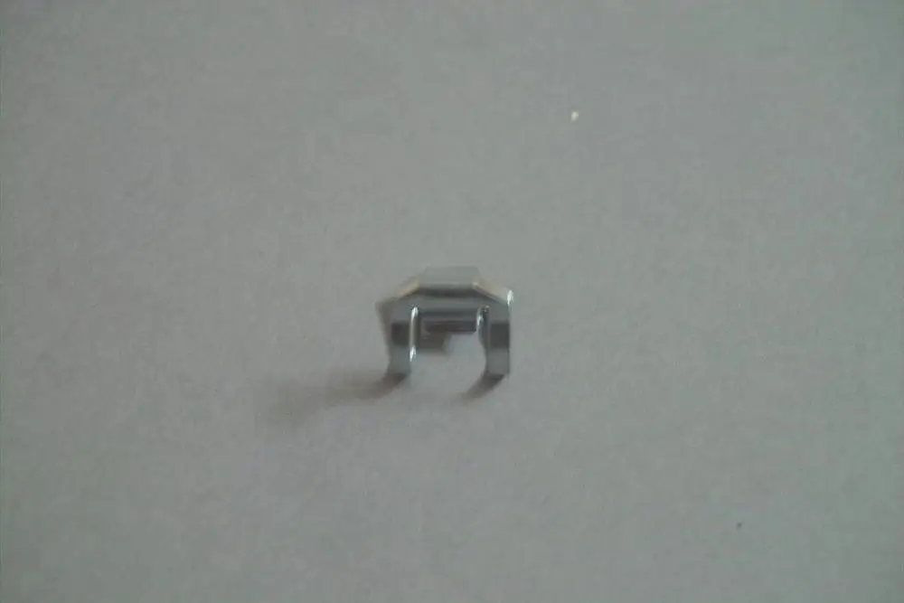 Brötje Verriegelungclip in metallischer Ausführung, zeigt eine kompakte Form mit zwei seitlichen Einkerbungen auf grauem Hintergrund.