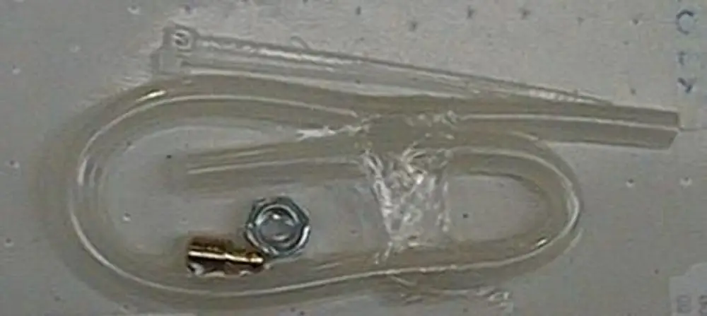 Luftschlauch von Brötje, transparent, gebogen. Enthält einen kleinen Metallteil und eine Mutter. Auf einer Oberfläche liegend, umgeben von Folie.