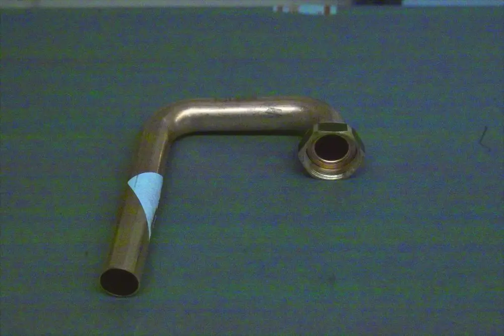 Brötje Vorlaufrohr mit einem gebogenen Ende und Anschluss zum Schrauben. Das Rohr hat eine metallische Oberfläche und liegt auf einer grauen Fläche.
